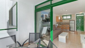 A modern apartment with a glass door leading to a balcony, a kitchenette, and a living area with a sofa and chairs.