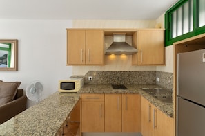 A compact kitchen with wooden cabinets, a granite countertop, a built-in microwave, and a stainless steel refrigerator.