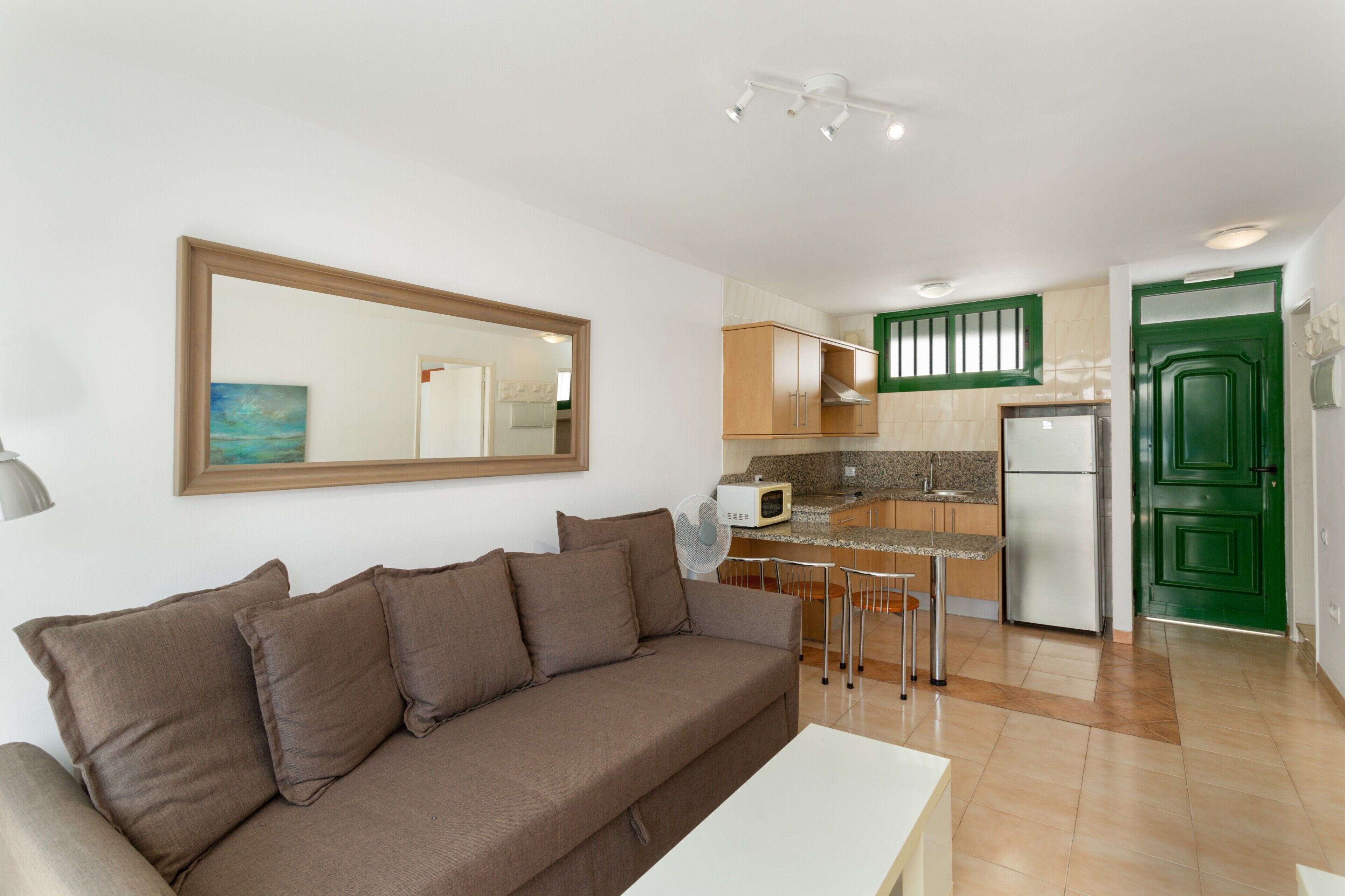 Sala de estar con sofá, mesa de comedor y área de cocina con microondas, refrigerador y armarios verdes.