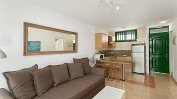 Sala de estar con sofá, mesa de comedor y área de cocina con microondas, refrigerador y armarios verdes.