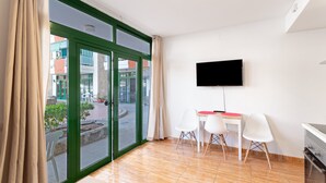 A room with a sliding glass door, a flat-screen TV mounted on the wall, a small table with chairs, and a built-in oven.