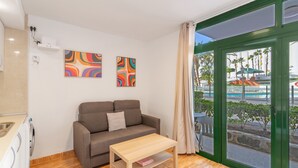 A modern room with a sofa, a small table, and a view of a pool and palm trees through a glass door.