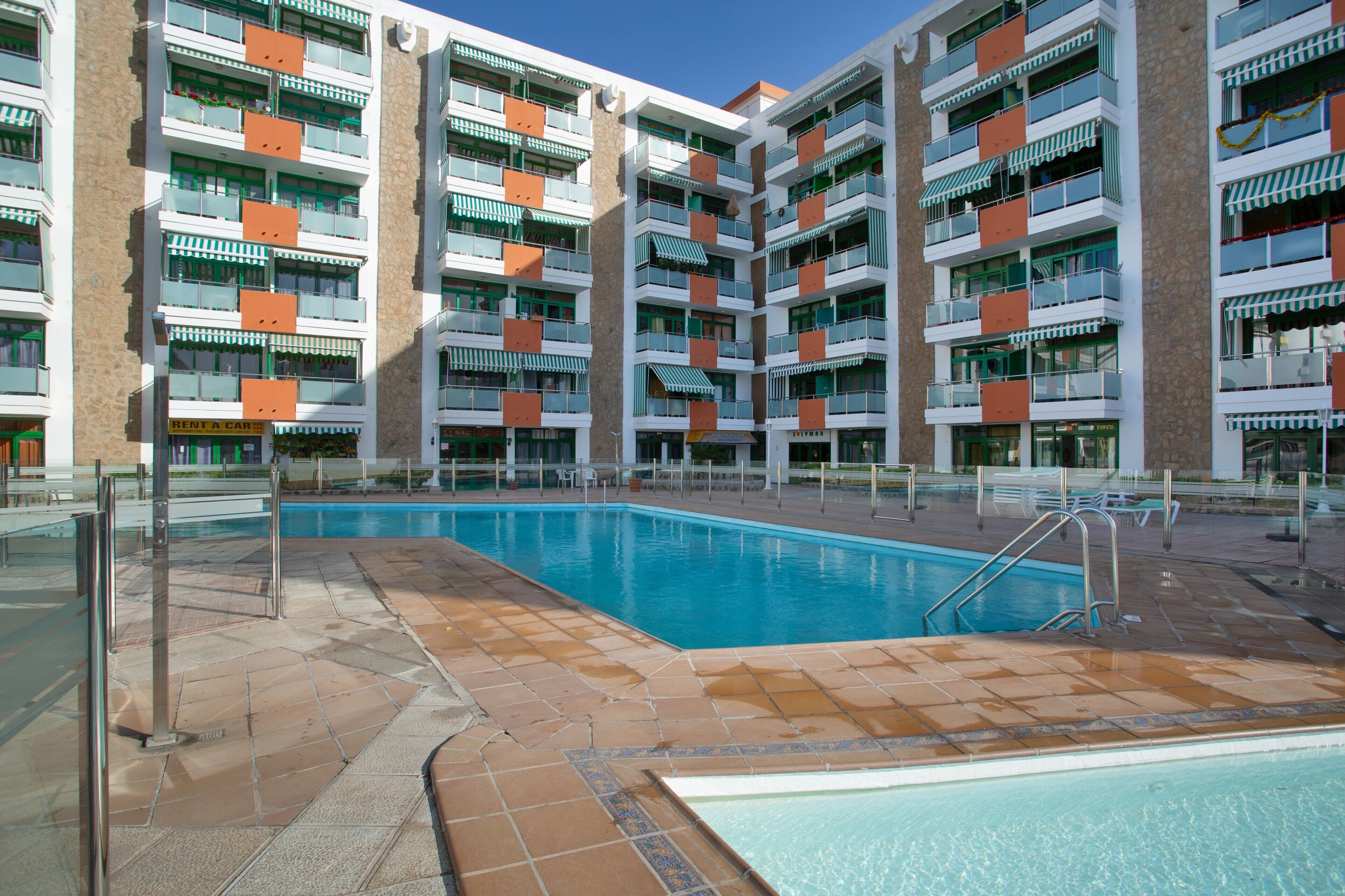 Ett hotell med flera våningar, en swimmingpool, balkonger och en skylt med texten ”HYR EN BIL”.