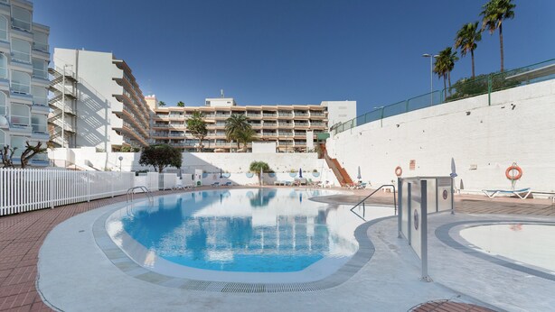Una piscina con agua cristalina azul, rodeada por un muro blanco y un camino de ladrillo.