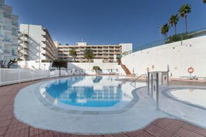 A swimming pool with a clear blue water, surrounded by a white wall and a brick walkway.