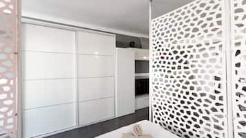 Une chambre moderne avec une armoire blanche, un panneau décoratif blanc et un lit bien fait, sur lequel est posée une serviette enroulée.