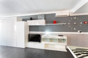 A modern kitchen with a flat-screen TV, white cabinetry, a built-in shelf, and a clock on the wall.