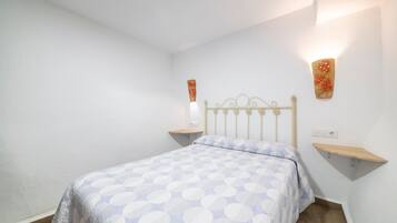A bedroom with a bed, a nightstand, a wall-mounted light, and a shelf.