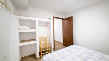 Un dormitorio con cama, una silla de madera, un armario y una puerta que da a otra habitación.