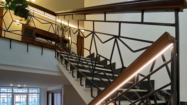 En moderne trappe med geometriske metalgelændere og et trægelænder, der fører op til en etage.