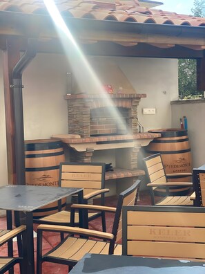 Un espace extérieur aménagé avec des tables et des chaises, un four en briques et des tonneaux en bois portant l’inscription « Piedemonte Bodega ».