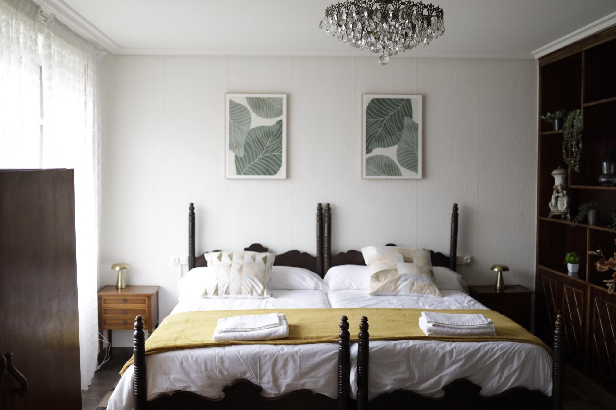 Una cama bien hecha con cabecera de madera, una mesita de noche con lámpara y una estantería con objetos decorativos.