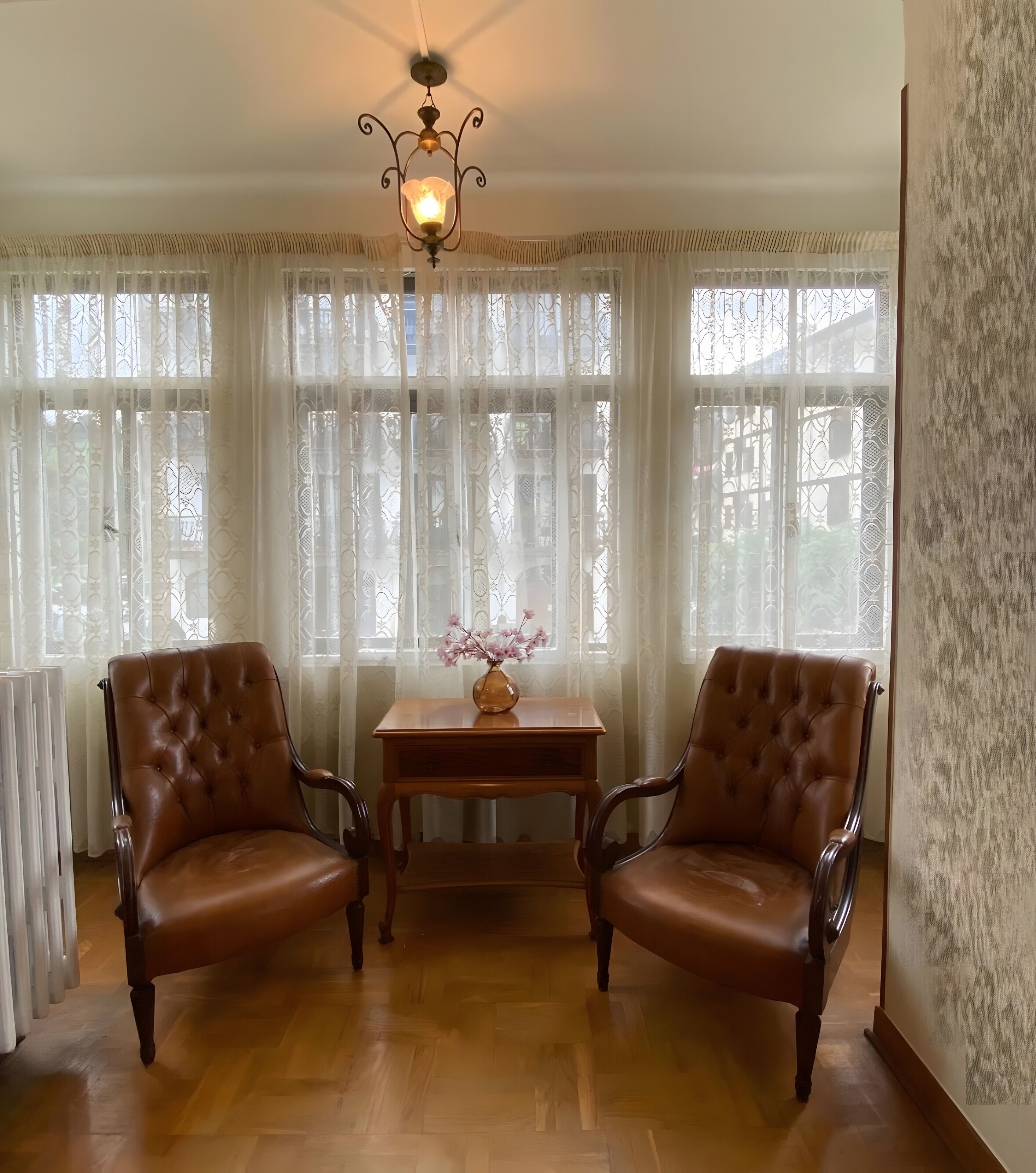 Een kamer met twee leren fauteuils, een houten tafel met een bloevas, en een kroonluchter.