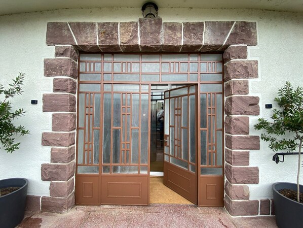 Une entrée encadrée de pierres, avec une grande porte en verre, des plantes en pot de chaque côté et un chemin bien visible menant à l’intérieur.