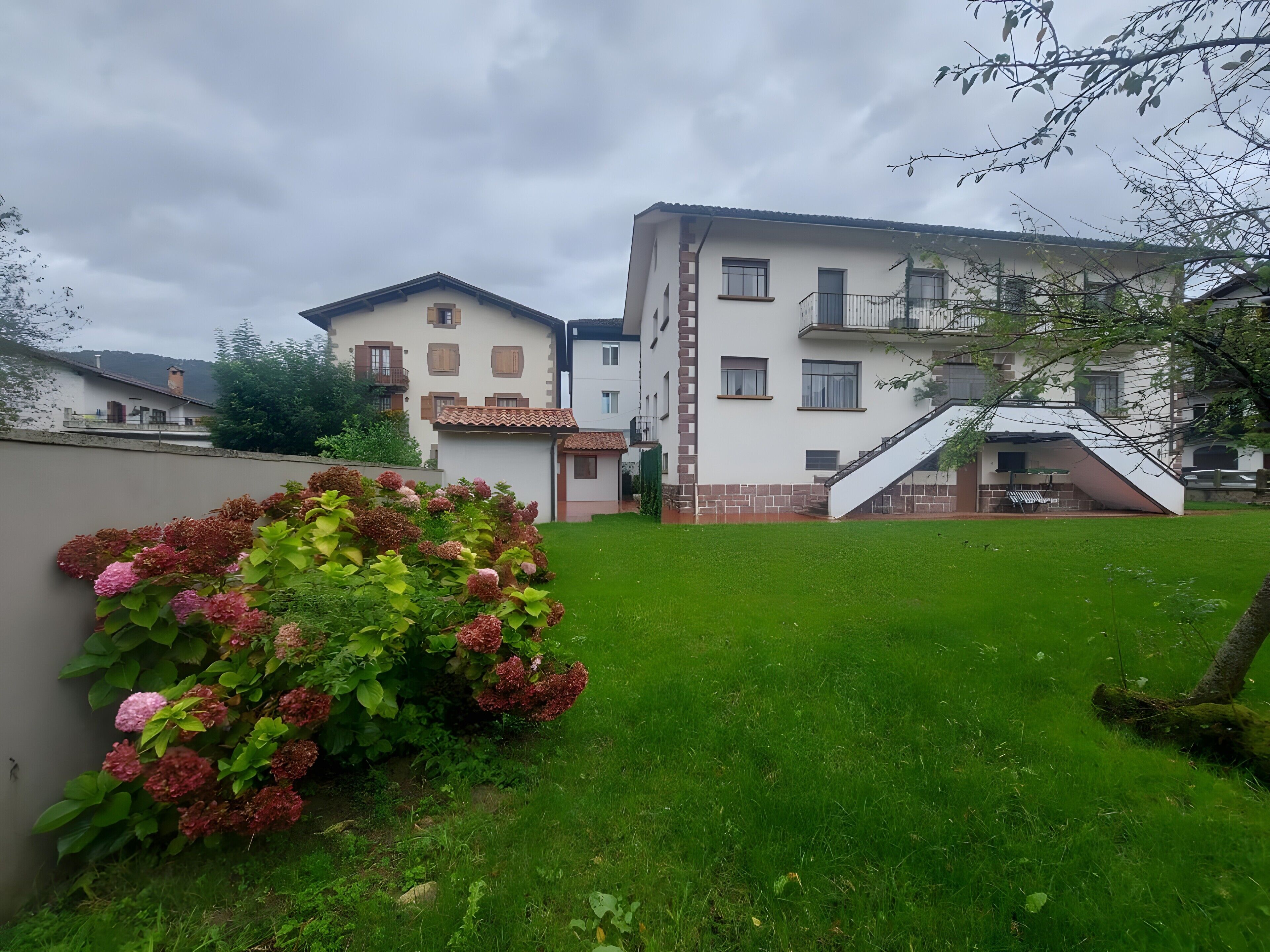 Un edificio residencial con un césped cuidado y un pequeño jardín de flores rosadas.