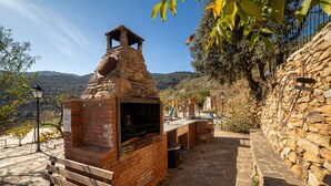 An outdoor brick oven with a chimney, a stone wall, and a bench.