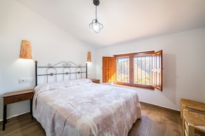 A bedroom with a bed, bedside tables, a window with wooden shutters, and a hanging light fixture.