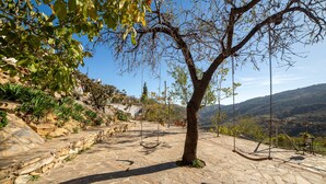 A stone pathway leading to a swing set, surrounded by trees and a mountainous backdrop.