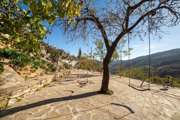 Un sendero de piedra que conduce a un conjunto de columpios, rodeado de árboles y un paisaje montañoso.