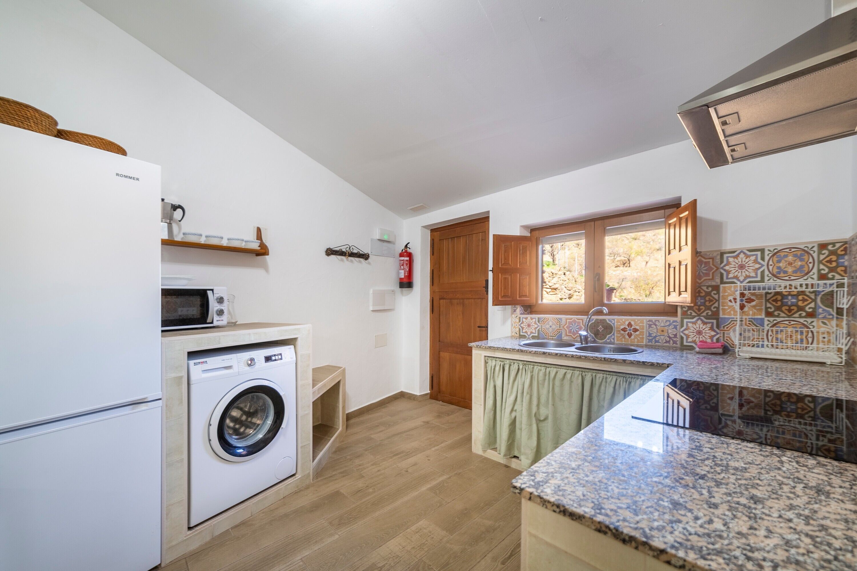A compact kitchen with a washing machine, a microwave, a sink, and a window with a view.
