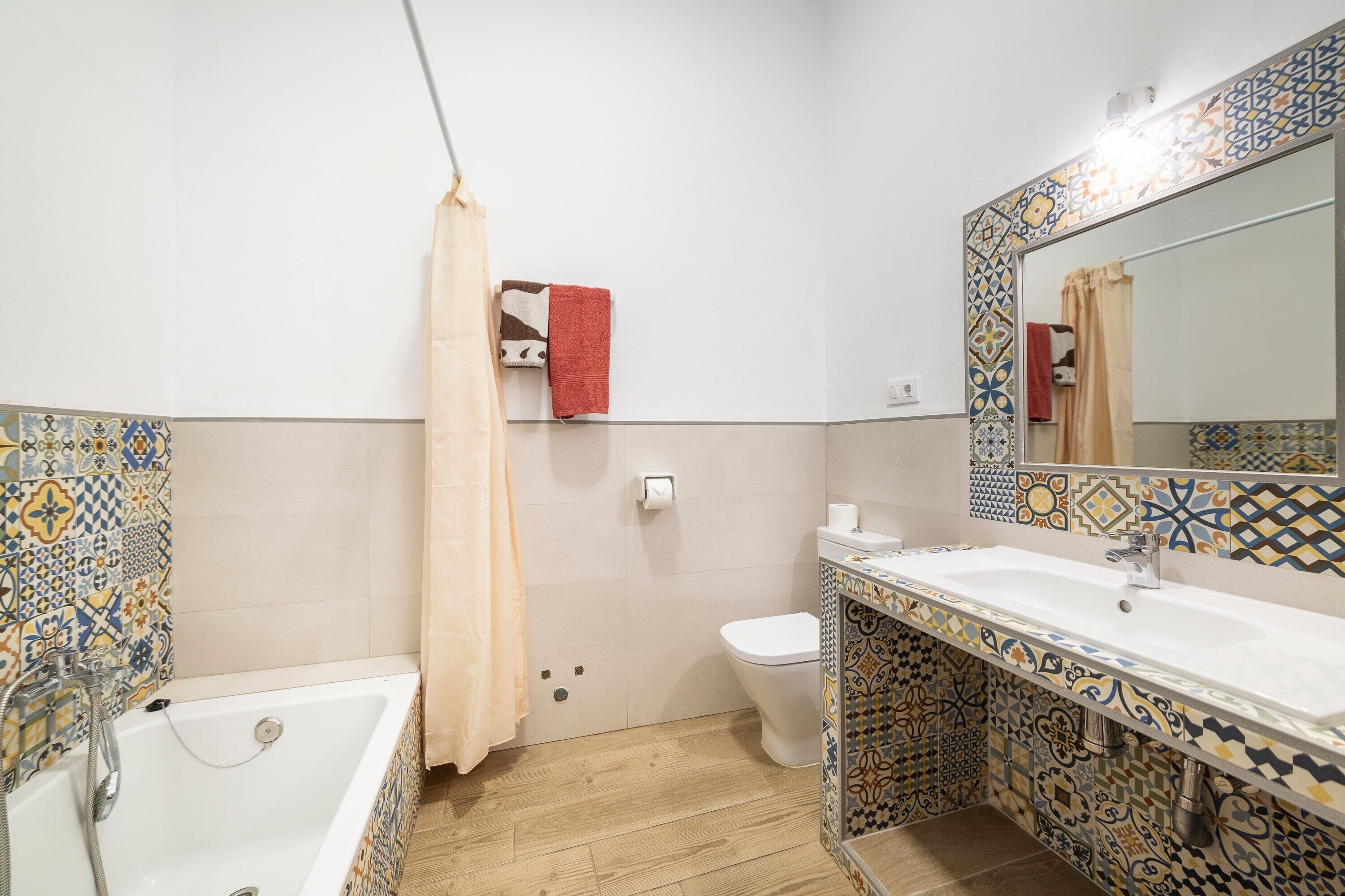 Un baño con bañera, inodoro y lavamanos, con baldosas estampadas y un espejo.