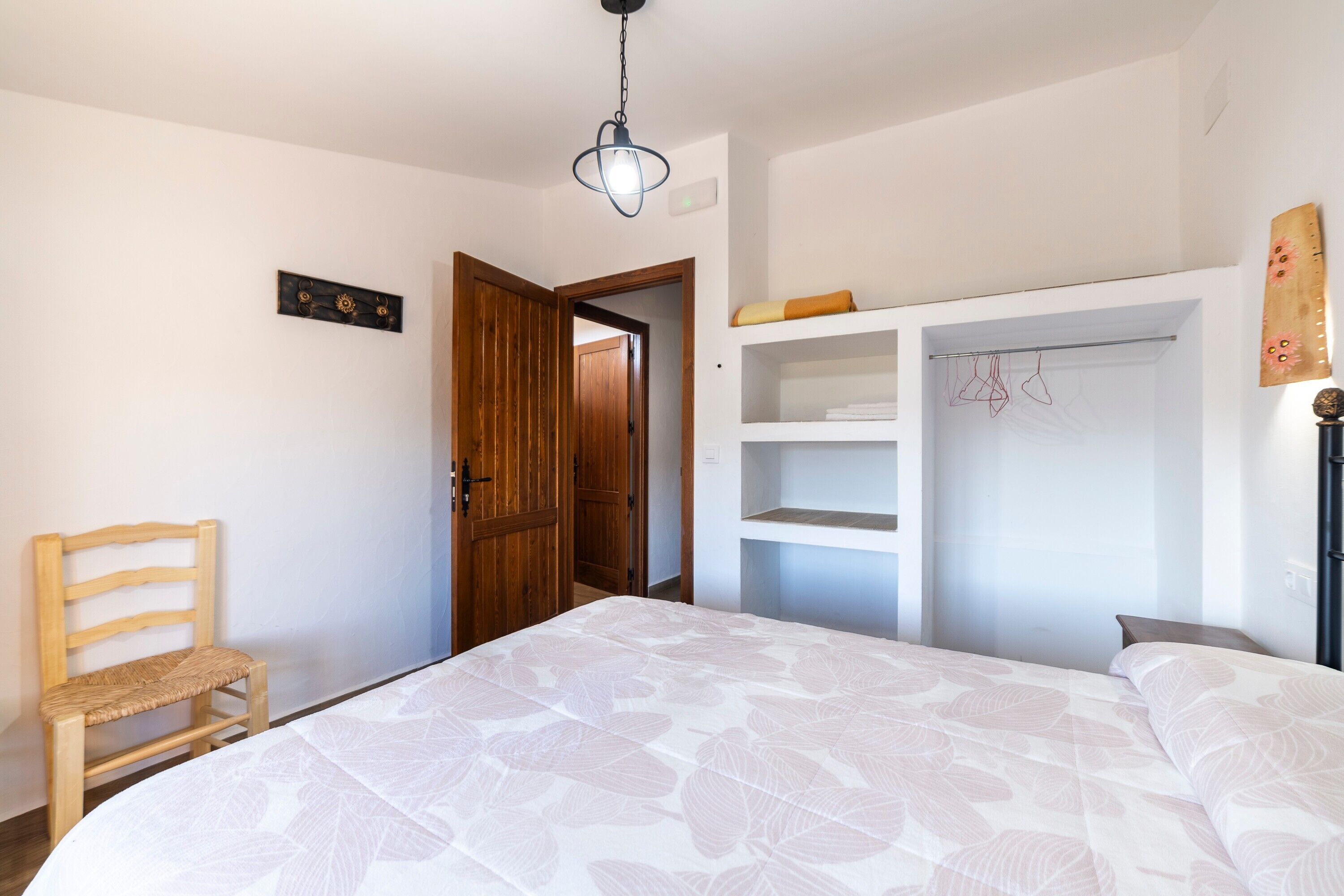 Une chambre à coucher comprenant un lit, une chaise en bois, une armoire et un luminaire suspendu.