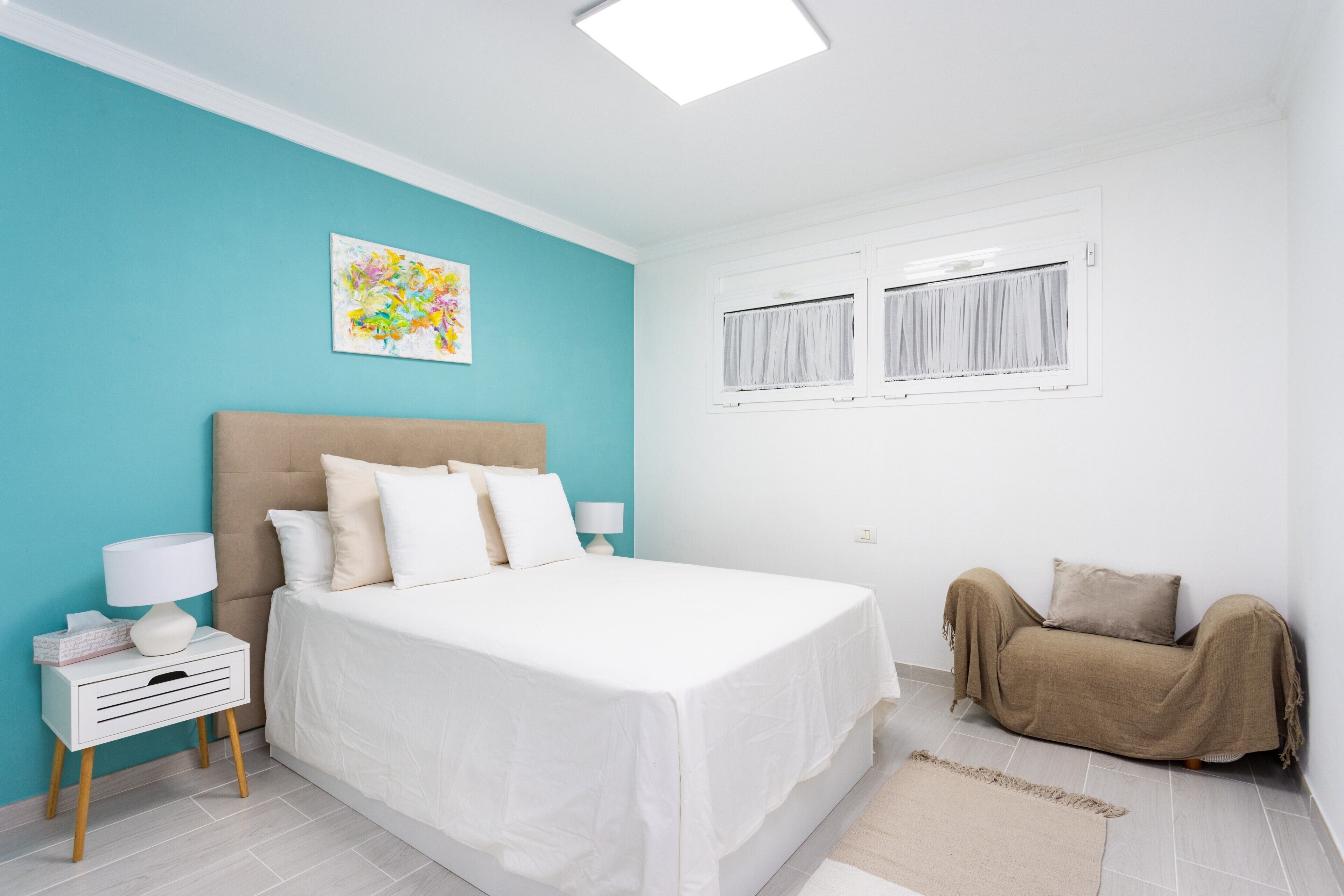 A bedroom with a bed, bedside tables, a window with curtains, a wall art piece, and a sofa.