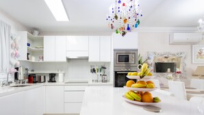 A modern kitchen with white cabinetry, a central island with fruit, and a decorative chandelier.