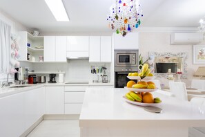 Une cuisine moderne avec des meubles blancs, un îlot central agrémenté de fruits et un lustre décoratif.