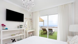 A bedroom with a large bed, a TV, a desk, and a view of a balcony with a chair.