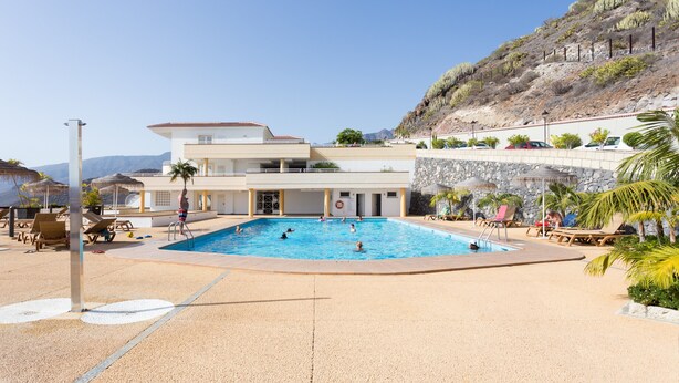 A swimming pool with lounge chairs and a building with a flat roof.