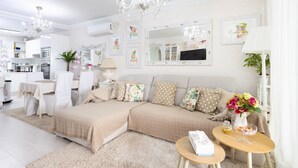 A modern living room with a sofa, a dining table, a chandelier, and a mirror.