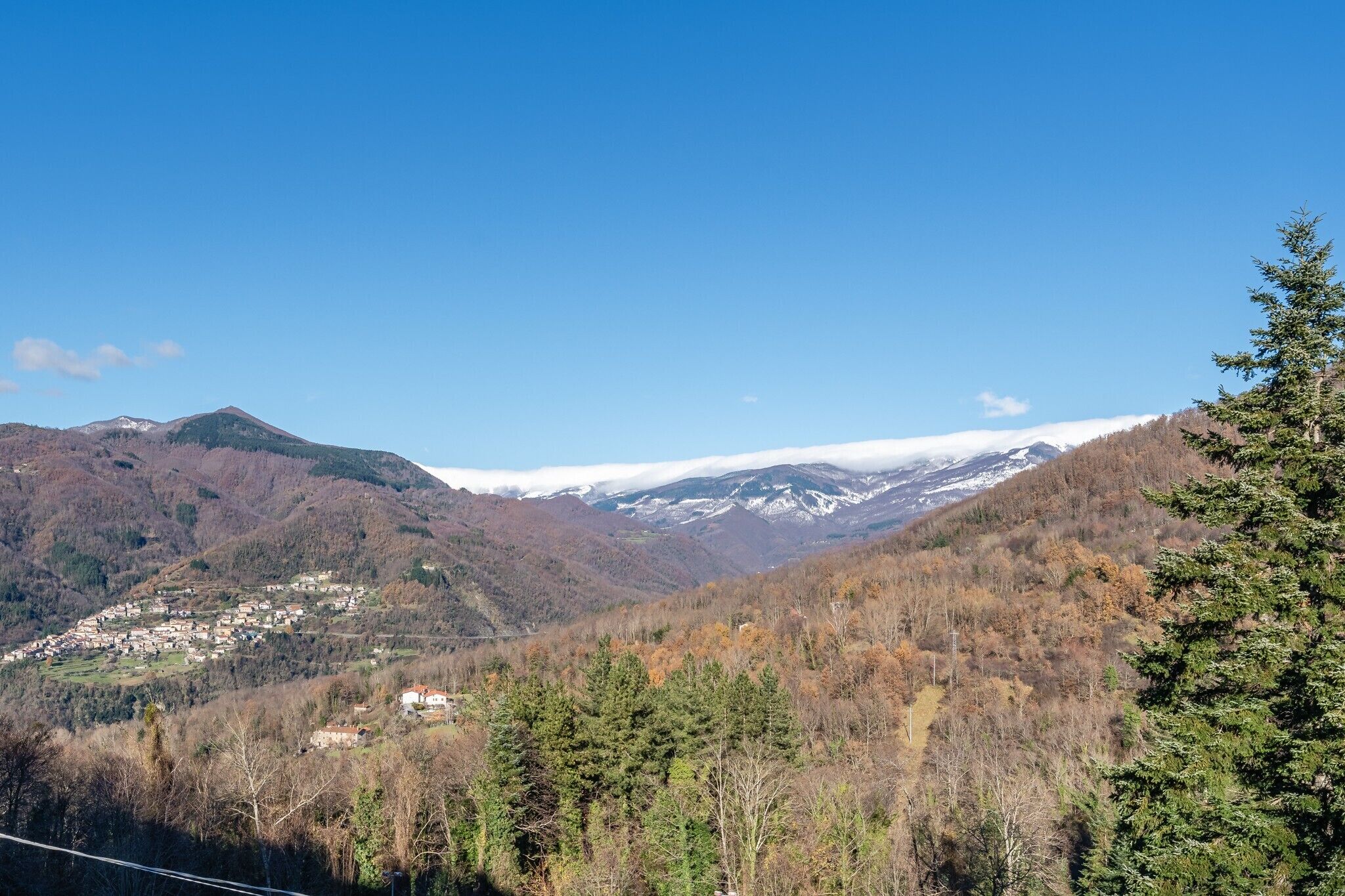 Paesaggio montuoso con un villaggio immerso nella valle, circondato da colline ricoperte di boschi.