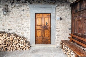 A rustic stone wall with a wooden double door, a wooden bench, and a stack of firewood.