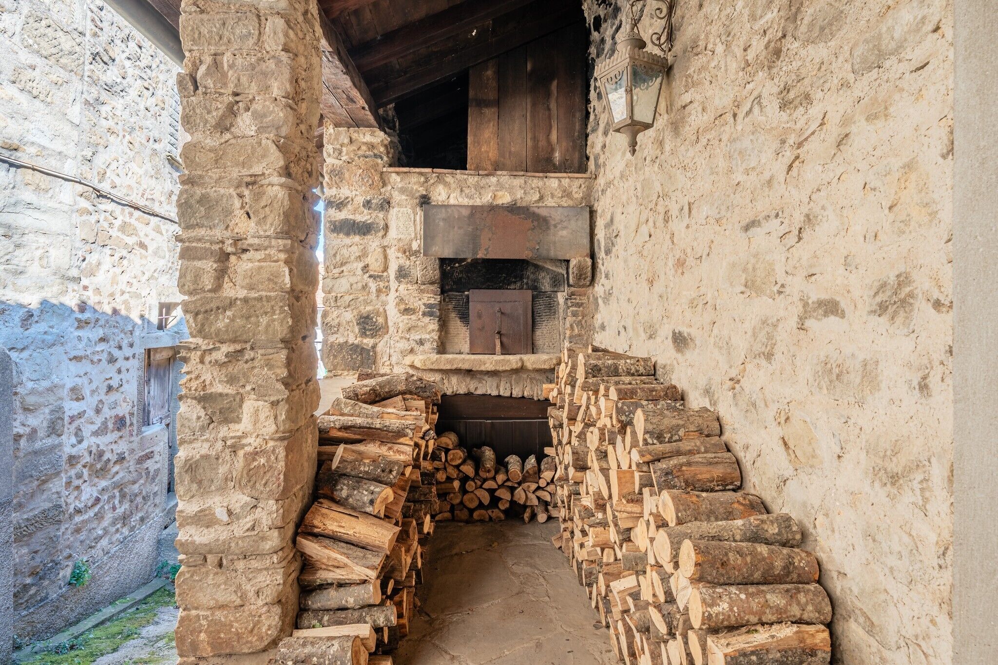 A stone-walled corridor with a fireplace, wooden logs, and a rustic interior.