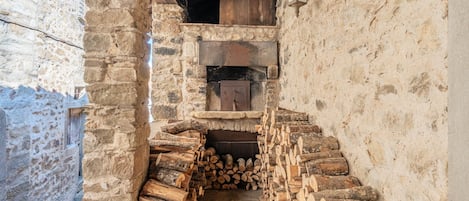 A stone-walled corridor with a fireplace, wooden logs, and a rustic interior.