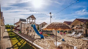 Een strand met een speelplaats, inclusief een glijbaan en een speelconstructie, en strandstoelen en parasols.