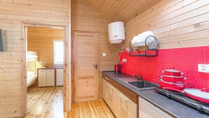 Een kleine keuken met houten wanden, een rode spatwand en basisvoorzieningen zoals een spoelbak, fornuis en afwasschaal.