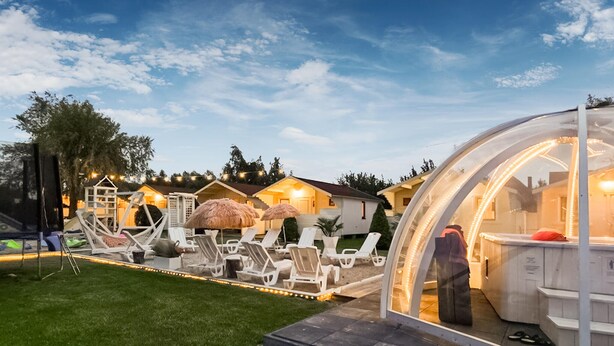 Een resort met een transparante koepelstructuur, terrasstoelen buiten en een goed verlicht patio.