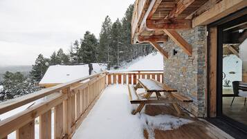 Una terraza de madera con un muro de piedra, un banco de madera y vistas a árboles cubiertos de nieve.