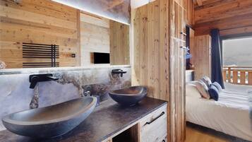Interior de una cabaña de madera con lavamanos doble, cama con almohadas y ventana con vistas.