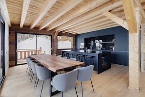 A wooden dining table with chairs, a kitchen area, and large windows with a view of a snowy landscape. - Chalet 'G2' with Lake View, Private Terrace and Wi-Fi (Les Angles)