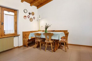 A dining area with a wooden table and chairs, a window with curtains, a radiator, and wall decorations including clocks and heart-shaped items. - Apartment 'Casa Pòlse' with Mountain View, Shared Garden and Wi-Fi (Baselga di Pinè)