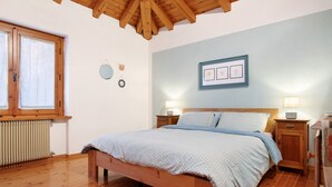 Ein Schlafzimmer mit einem hölzernen Bett, Nachttischen mit Lampen, einem Heizkörper und einem Fenster mit Vorhängen.
