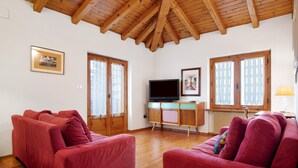 Ein Zimmer mit Holzboden, einem roten Sofa, einem Fernseher und einem Schreibtisch mit Computer.