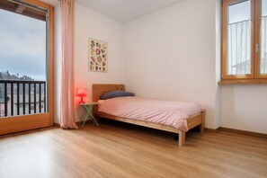 A bedroom with a wooden bed, a nightstand with a lamp, a window with curtains, and a wall art piece.