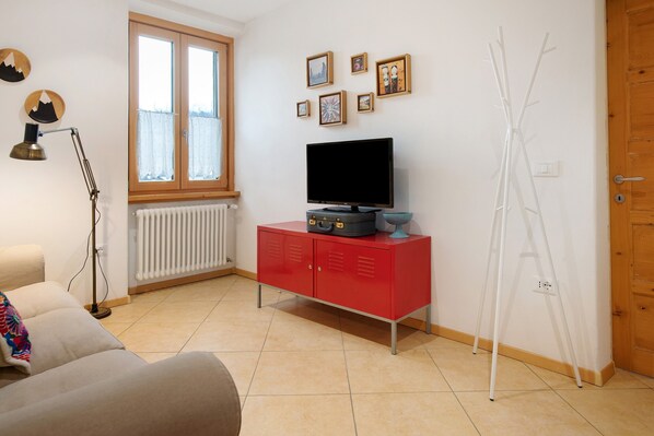 Un salon avec un meuble rouge, un téléviseur, un radiateur, une fenêtre et un porte-manteau.