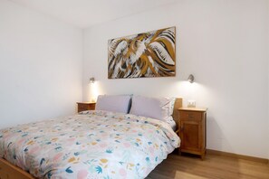 A bedroom with a bed, two bedside tables, a wall-mounted painting, and a nightstand.