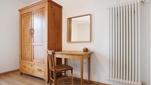 Une pièce comprenant une armoire en bois, un bureau en bois avec une chaise, un miroir et un radiateur blanc.