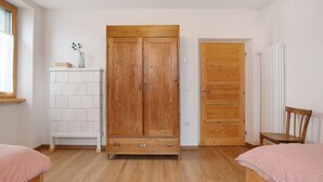 Une chambre avec une armoire en bois, un banc blanc, une chaise en bois et un lit recouvert d’une couvre-lit à motifs.